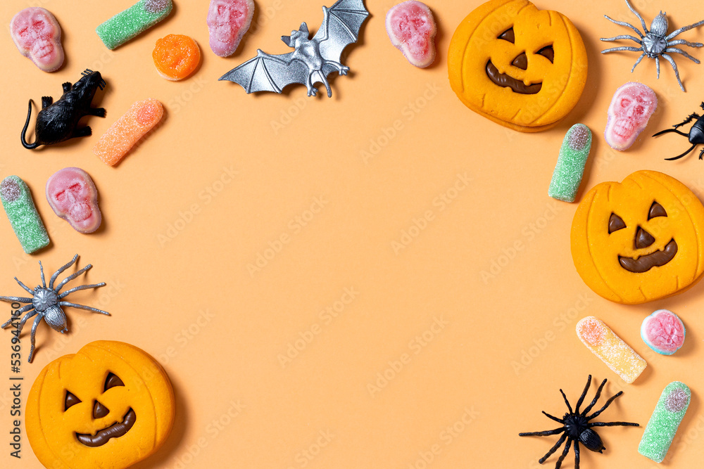 Halloween sweet background frame with scary pumpkin cookies, candy and Halloween decor on orange table