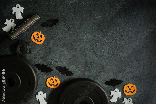 Dumbbell barbell weight plates and Halloween decorations - pumpkins, bats and ghosts. Healthy fitness lifestyle autumn fall flat lay composition. Gym workout sport training concept with copy space.