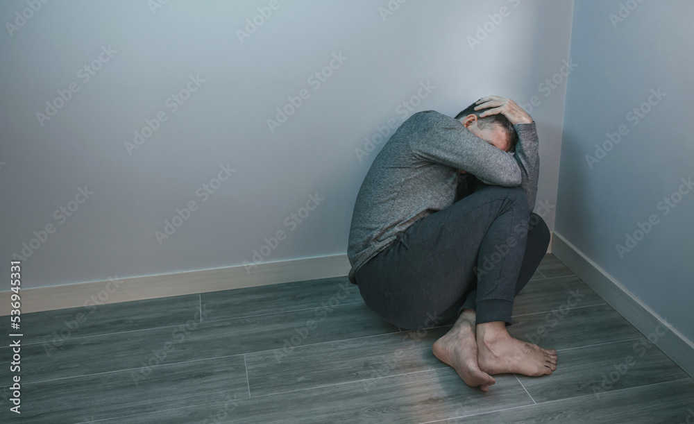 Unrecognizable man with problems holding his head in hands sitting in the corner of room