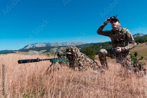Sniper soldier assisted by an assistant to observe the area to be targeted with modern warfare tactical virtual reality goggles aerial drone military technology. © .shock