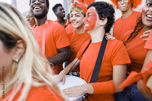 Orange sport fans screaming while supporting their team out of the stadium - Football supporters having fun at competion event - Focus on right girl face