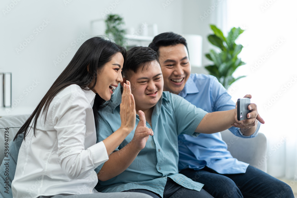Asian young parents and down syndrome son use phone video call at home. Asian young parents and down syndrome son use phone video call at home.