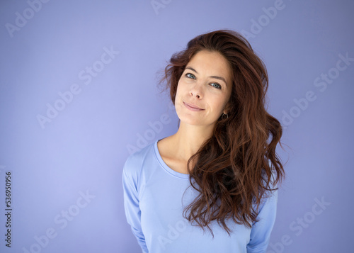 athletic woman with purple shirt in front of purple background with long dark hair
