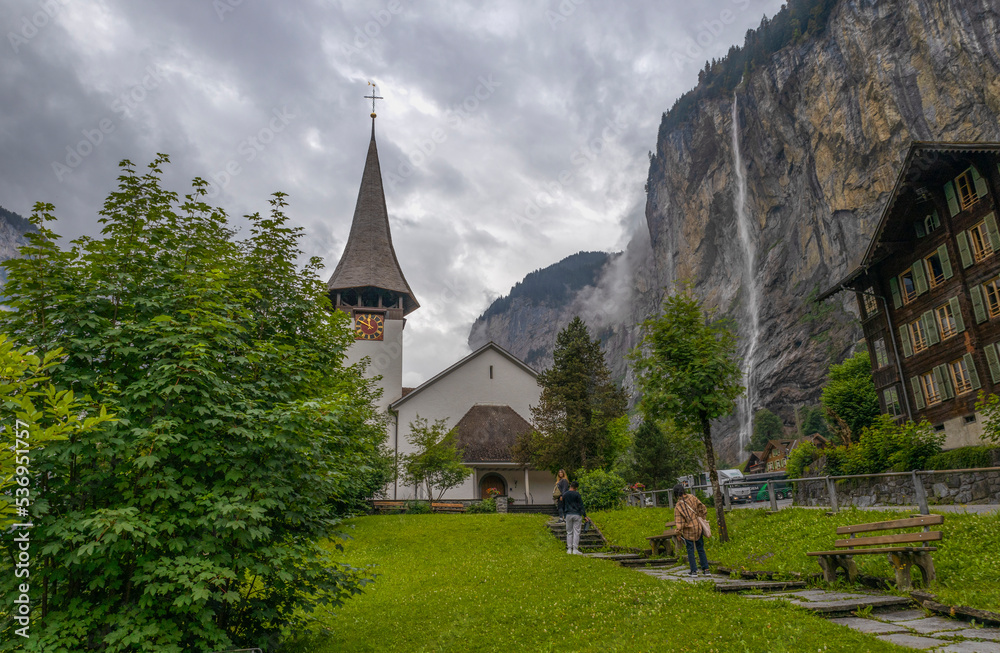 LAUTERBRUNNEN, SWITZERLAND, JUNE 22, 2022 - The church in the alpine town of Lauterbrunnen with the The Staubbach waterfall, in Bernese Oberland, Switzerland.