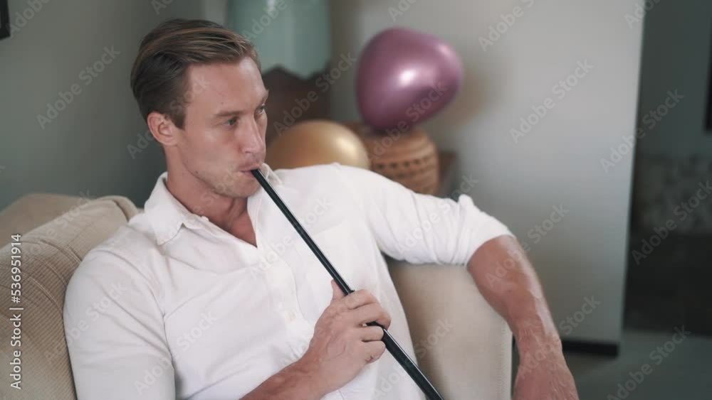 Slowmotion video of Caucasian young man smoking hookah on sofa. Strong