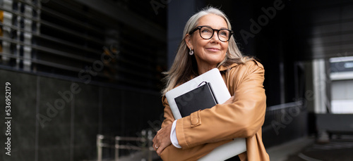 portrait of an elderly businesswoman with a laptop in glasses outside the office, strong and independent woman concept
