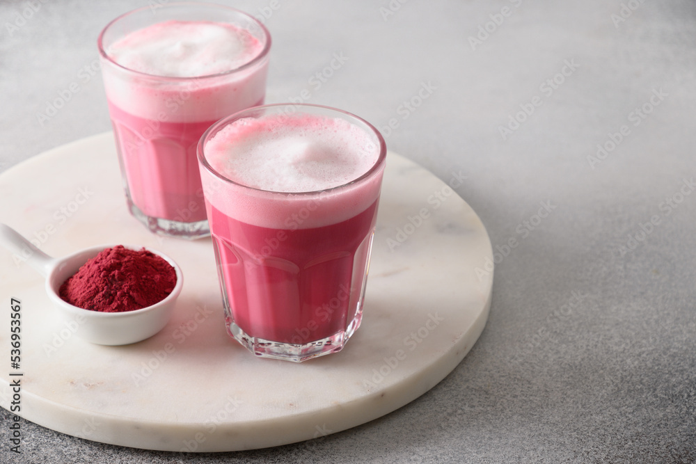 Beetroot latte or pink moon milk latte in glasses of beetroot powder and vegan milk on gray background. Trendy healthy vegan drink. Close up. Copy space. Beetroot latte or pink moon milk latte in glasses of beetroot powder and vegan milk on gray background. Trendy healthy vegan drink. Close up. Copy space.