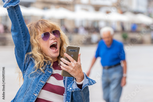 middle-aged woman excited with joy on the street with mobile phone photo