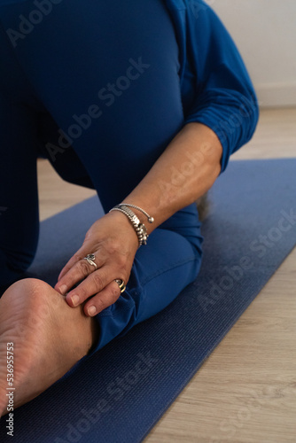 Yoga teacher dressed in blue touches her ankles during stretching.