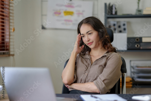 Asian businesswoman sitting in the office feeling tired, stressed or exhausted from a long day at work. © amnaj