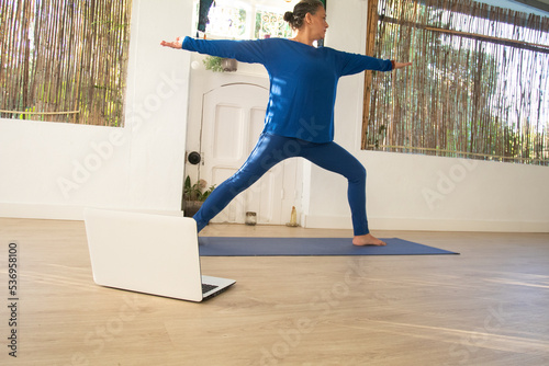 Fotografia The yoga teacher, dressed in blue, stretches her arms as she leads an online class from her home