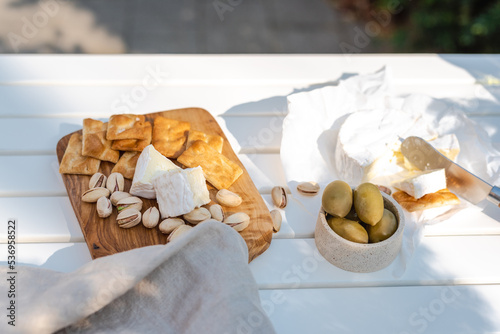 Schilderij op canvas Wine appetizers namely pistachios, camembert cheese, saltine crackers and olives on a white table outdoors