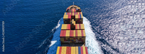 Aerial drone ultra wide top down photo of container cargo tanker ship carrying truck-size colourful containers in deep blue open ocean sea 