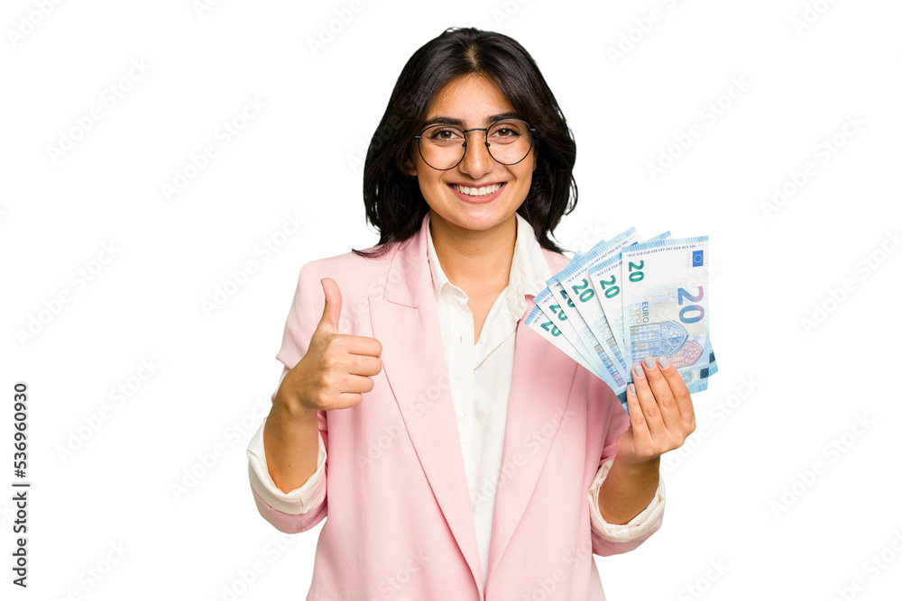 Young business Indian woman holding banknotes isolated smiling and raising thumb up Young business Indian woman holding banknotes isolated smiling and raising thumb up
