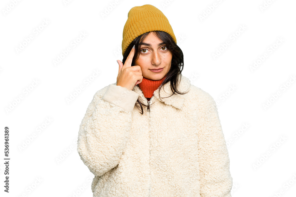Young Indian woman wearing winter jacket and a wool cap isolated pointing temple with finger, thinking, focused on a task. Young Indian woman wearing winter jacket and a wool cap isolated pointing temple with finger, thinking, focused on a task.