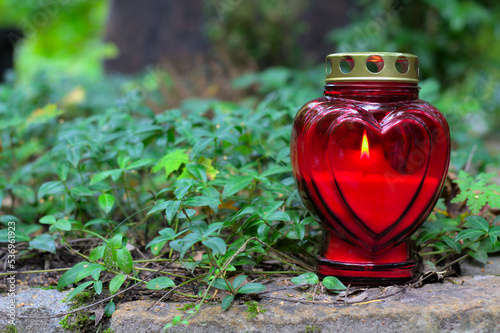 A red heart-shaped candle on a grave in a cemetery. All Saints Day. Copy space, shallow depth of field.