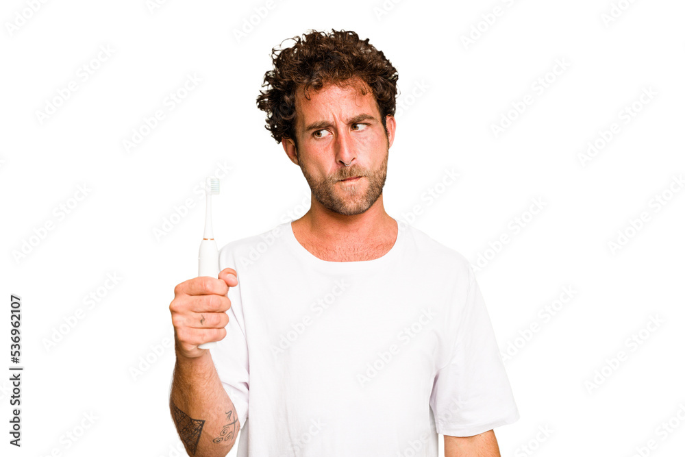 Young caucasian man holding an electric toothbrush isolated confused, feels doubtful and unsure. Young caucasian man holding an electric toothbrush isolated confused, feels doubtful and unsure.