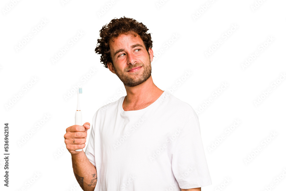 Young caucasian man holding an electric toothbrush isolated looks aside smiling, cheerful and pleasant. Young caucasian man holding an electric toothbrush isolated looks aside smiling, cheerful and pleasant.