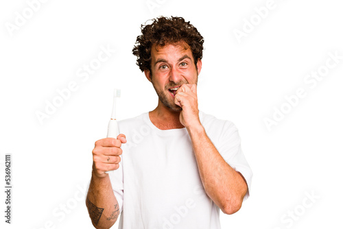 Young caucasian man holding an electric toothbrush isolated biting fingernails, nervous and very anxious.