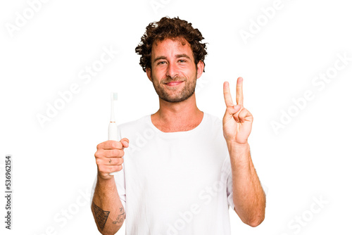 Young caucasian man holding an electric toothbrush isolated showing number two with fingers.