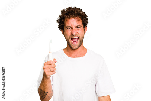 Young caucasian man holding an electric toothbrush isolated screaming very angry and aggressive.
