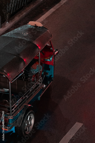 Nighttime view of a Tuk-Tuk vehicle with a wet roof driving in Bangkok, Thailand