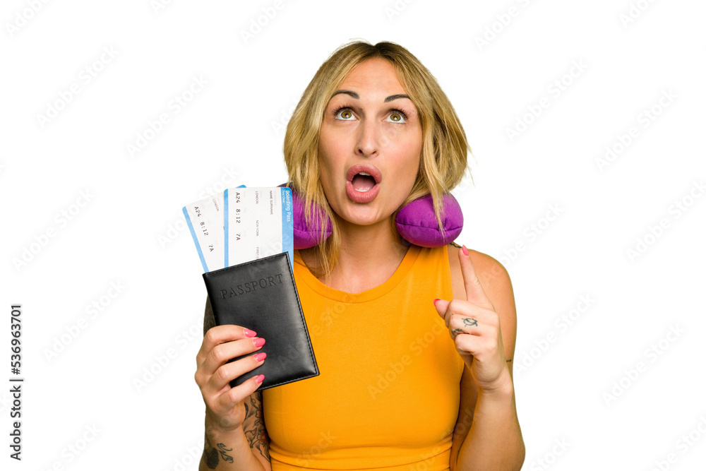 Young caucasian woman with inflatable travel pillow holding passport isolated on green chroma background pointing upside with opened mouth. Young caucasian woman with inflatable travel pillow holding passport isolated on green chroma background pointing upside with opened mouth.