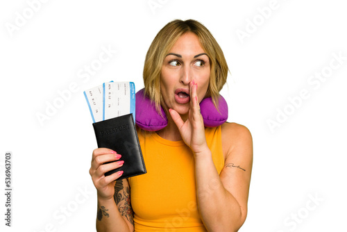 Young caucasian woman with inflatable travel pillow holding passport isolated on green chroma background is saying a secret hot braking news and looking aside