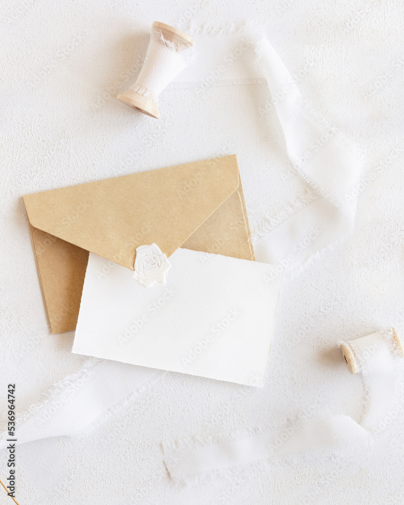 Card and envelope near silk ribbons top view on white, romantic wedding mockup
