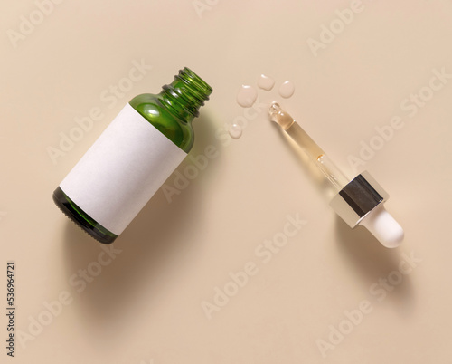Opened Green dropper bottle with blank label on light beige top view, cosmetic Mockup