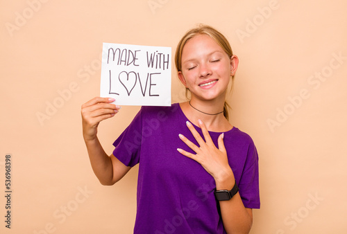 Little caucasian girl holding made with love placard isolated on beige background