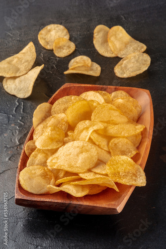 Potato chips or crisps in a wooden bowl on a black slate background