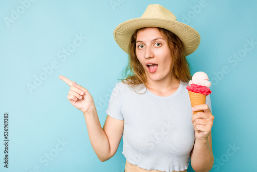 Young caucasian woman holding an ice cream isolated a blue background pointing to the side