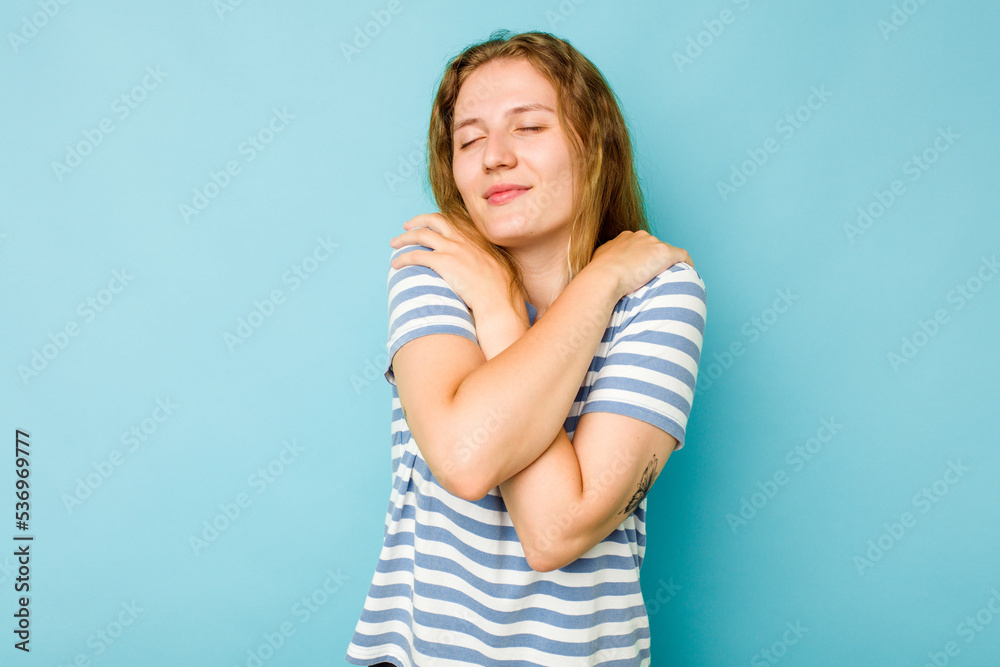 Young caucasian woman isolated on blue background hugs, smiling carefree and happy.