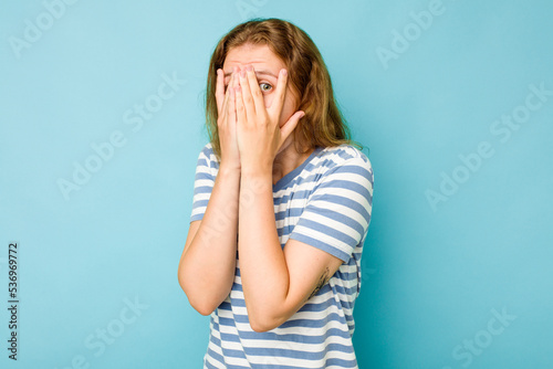 Young caucasian woman isolated on blue background blink through fingers frightened and nervous.