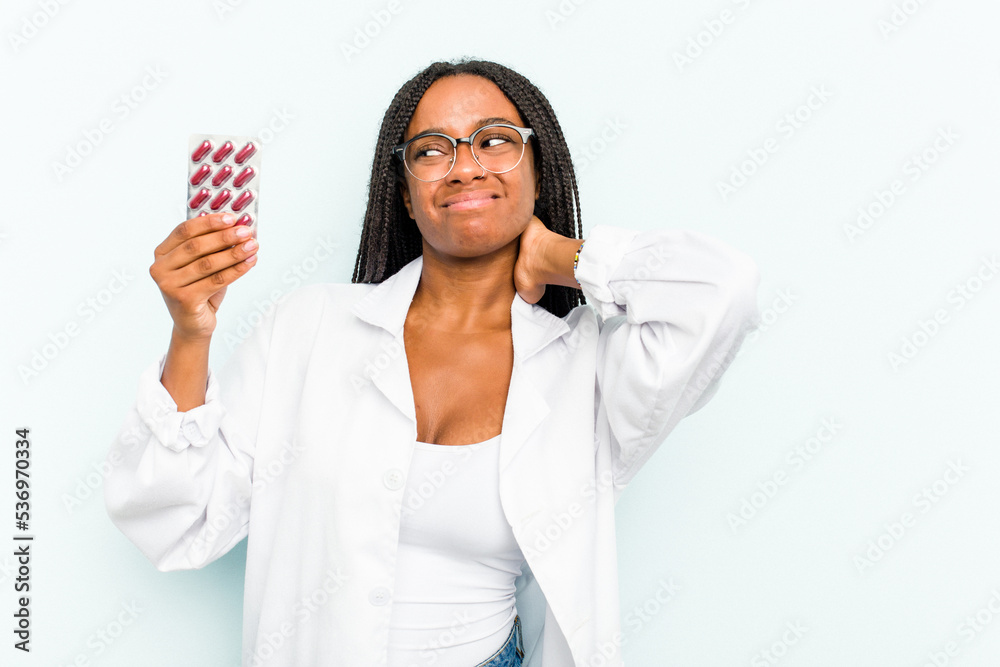Young African American pharmacist woman isolated on blue background touching back of head, thinking and making a choice. Young African American pharmacist woman isolated on blue background touching back of head, thinking and making a choice.