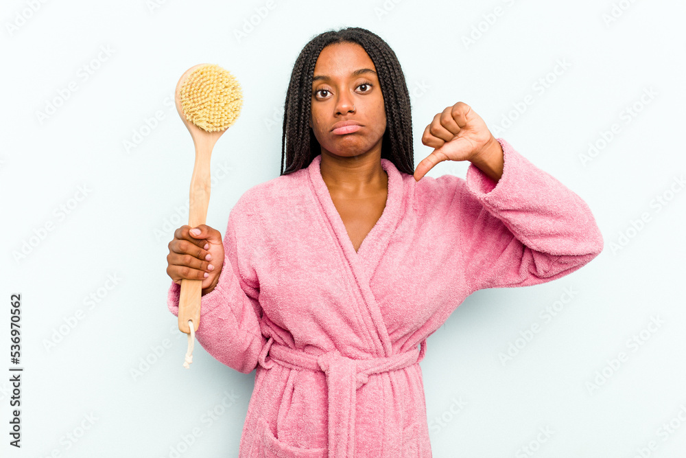 Young African American woman holding a bathtub brush isolated on blue background showing a dislike gesture, thumbs down. Disagreement concept. Young African American woman holding a bathtub brush isolated on blue background showing a dislike gesture, thumbs down. Disagreement concept.
