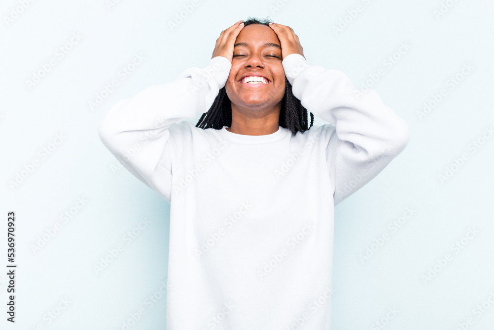 Young African American woman with braids hair isolated on blue background laughs joyfully keeping hands on head. Happiness concept. Young African American woman with braids hair isolated on blue background laughs joyfully keeping hands on head. Happiness concept.