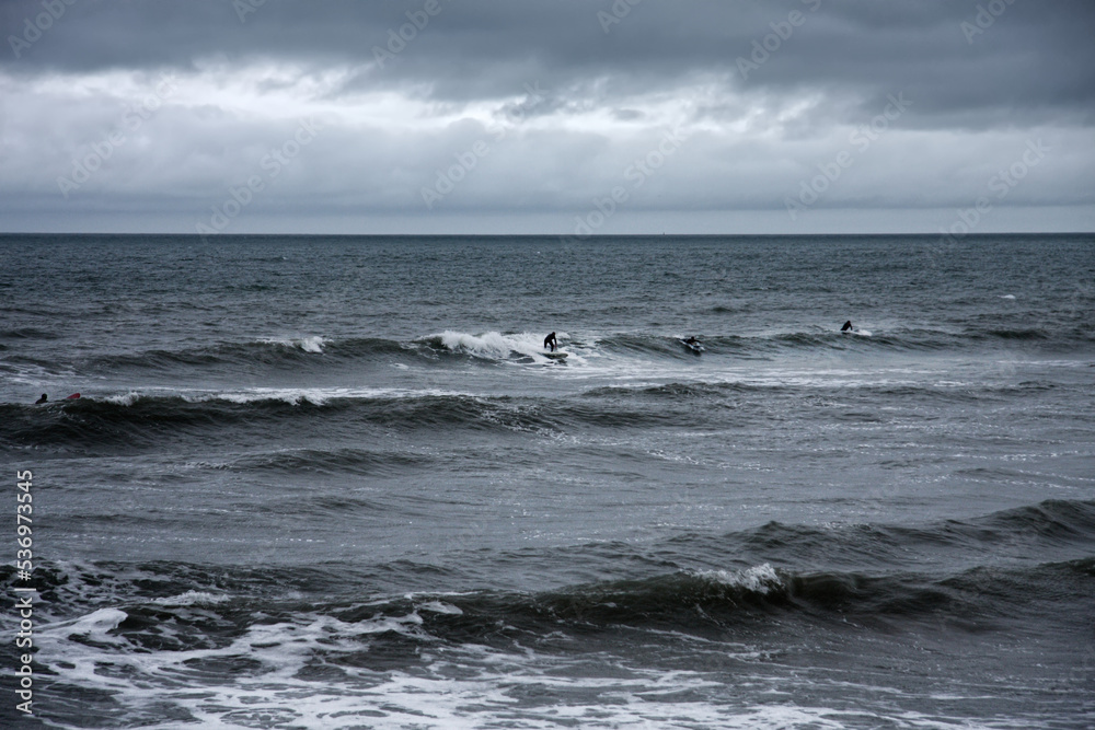 all weather surfers surf waves on grey day at british seaside
