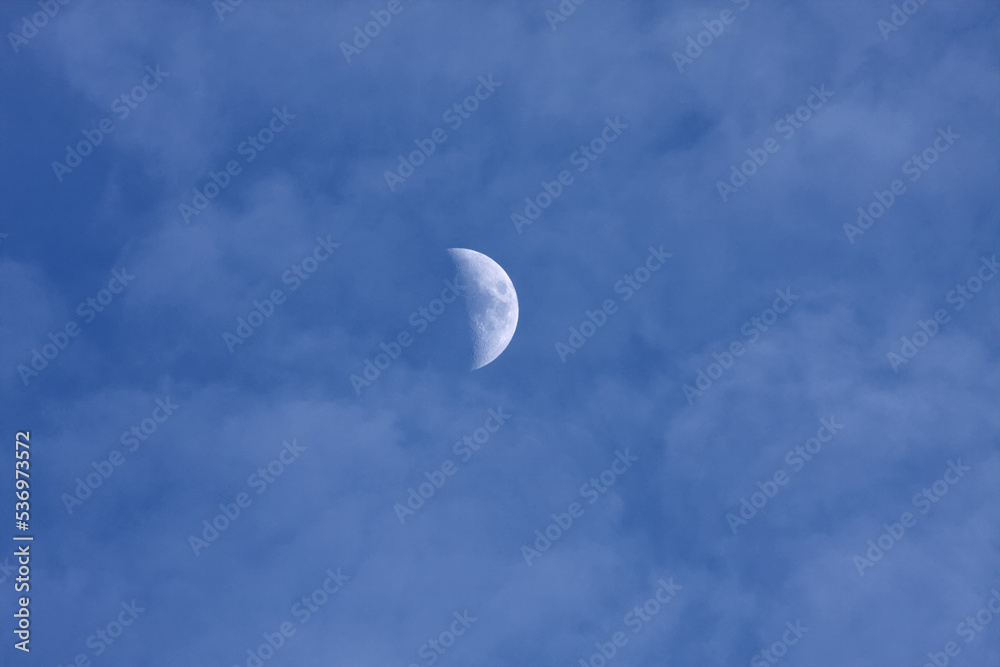 half moon in late afternoon cloudy blue sky
