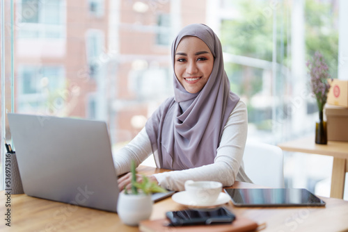 A beautiful Muslim woman with a smiling face in the morning drinking coffee and using a computer