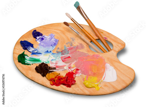 Wooden art palette with blobs of paint and a brushes on white background photo