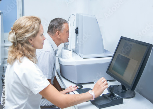 an elderly man on a CT scanner does a retinal tomography in the oculist's office. brain, a female optometrist is sitting at a computer..