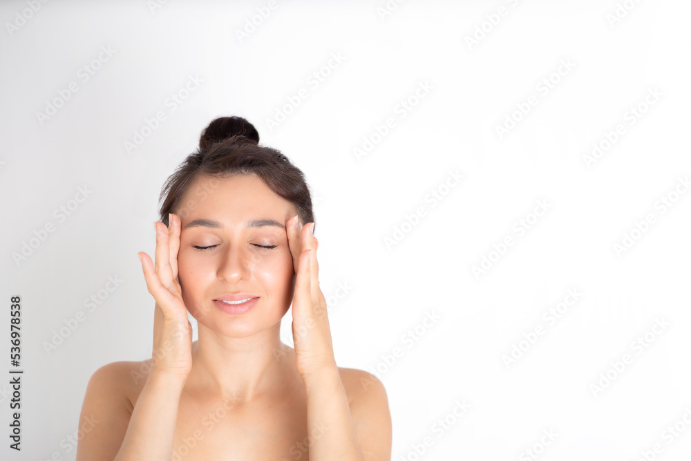 A young beautiful brunette woman massages her face and neck. The naturalness of self-care. White background place for text A young beautiful brunette woman massages her face and neck. The naturalness of self-care. White background place for text