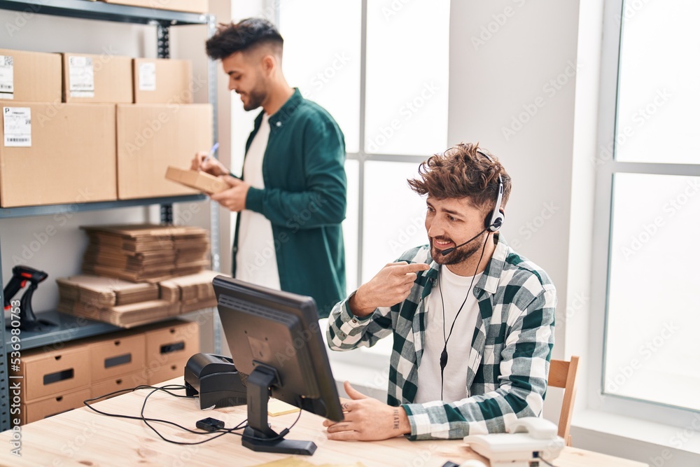 Two hispanic men working at small business ecommerce smiling happy pointing with hand and finger Two hispanic men working at small business ecommerce smiling happy pointing with hand and finger
