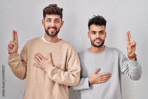 Canvastavla Young homosexual couple standing over white background smiling swearing with han