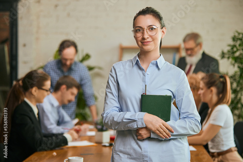 Portrait of young and successful business lady. Happy smart girl in business suit in modern office during meeting with colleagues
