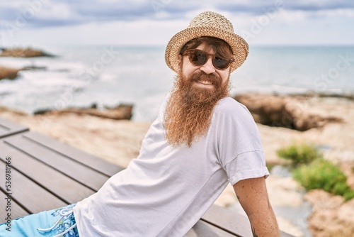 Young redhead tourist man smiling happy sitting on the bench at the beach.