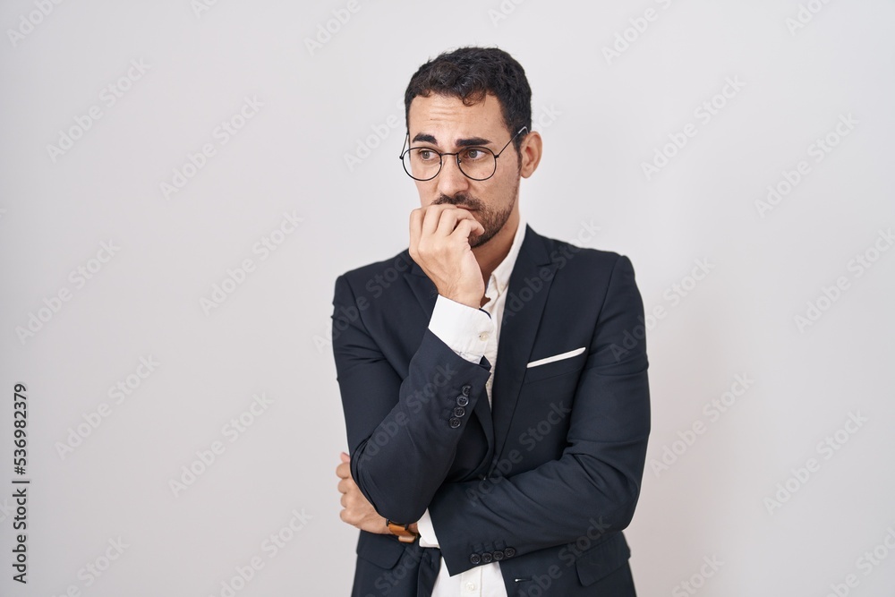 Handsome business hispanic man standing over white background looking stressed and nervous with hands on mouth biting nails. anxiety problem. Handsome business hispanic man standing over white background looking stressed and nervous with hands on mouth biting nails. anxiety problem.