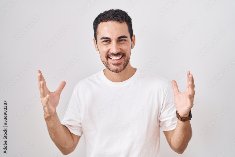 Handsome hispanic man standing over white background celebrating mad and crazy for success with arms raised and closed eyes screaming excited. winner concept Handsome hispanic man standing over white background celebrating mad and crazy for success with arms raised and closed eyes screaming excited. winner concept